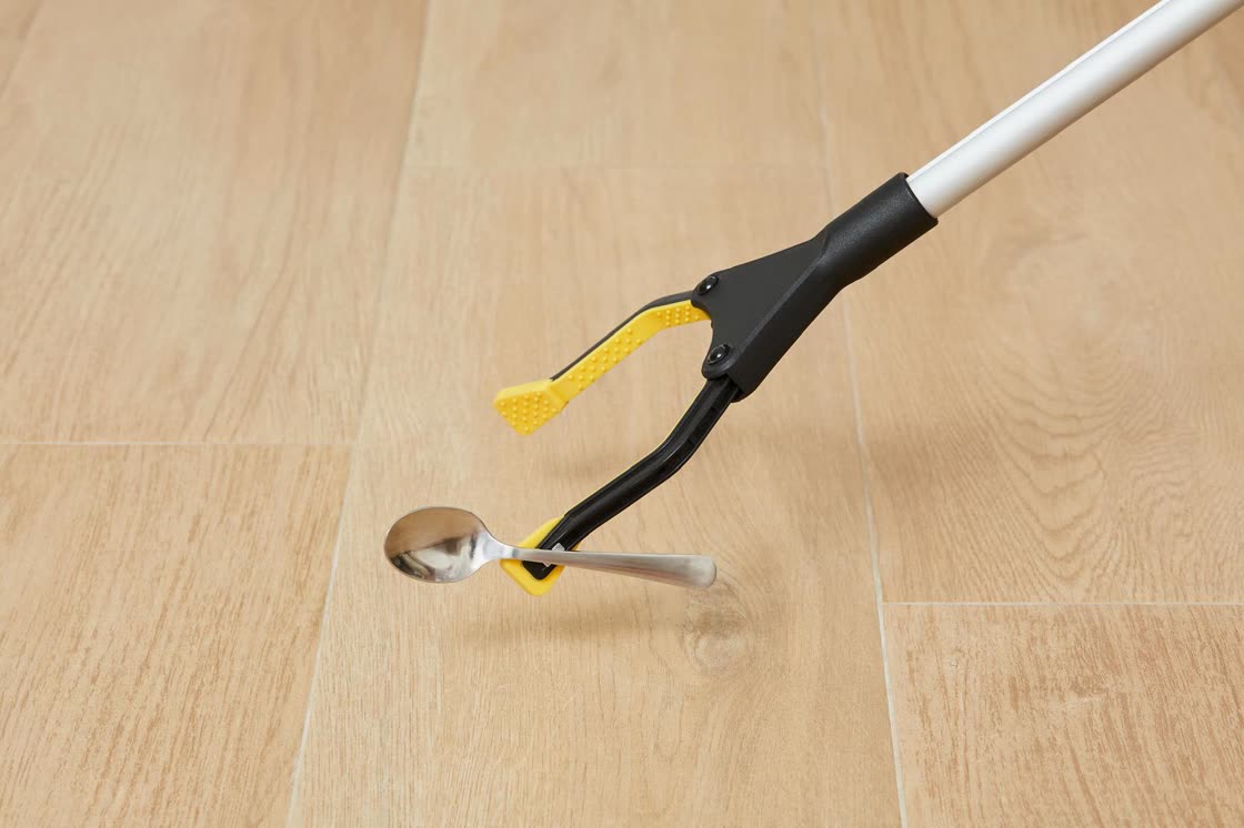 La mordaza de la pinza cierra sobre una cuchara caída en el suelo de madera.