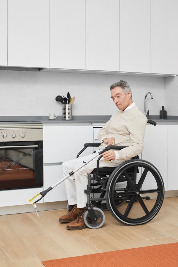 Un hombre en silla de ruedas sostiene la cuchara que acaba de recoger del suelo.